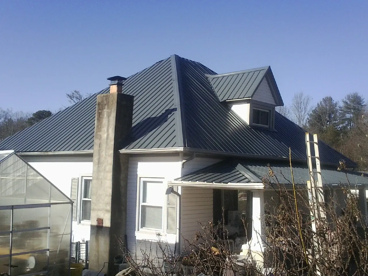Dark blue standing seam metal roof on a white farmhouse with dormer — Slate & Tile Roof Repair by Roofing Brothers in Burkeville