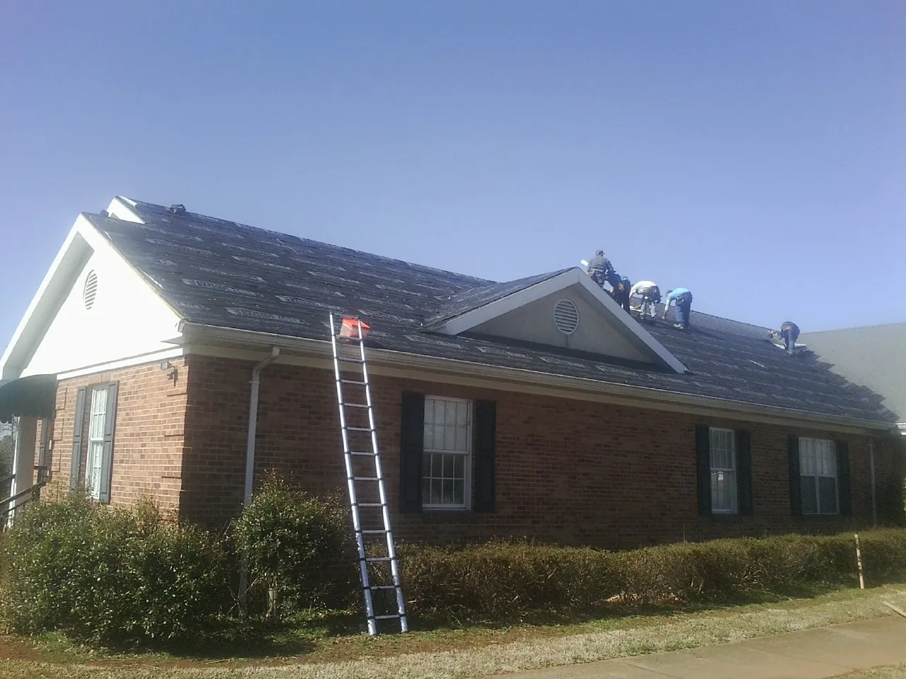 Crew tearing shingles off a brick ranch roof with a ladder set — Metal Roof Repair work by our crew in Burkeville