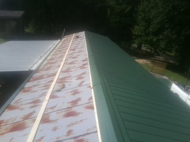 Old rusted panels beside newly installed green metal roofing — Wind Damage Roof Repair by Roofing Brothers in Burkeville