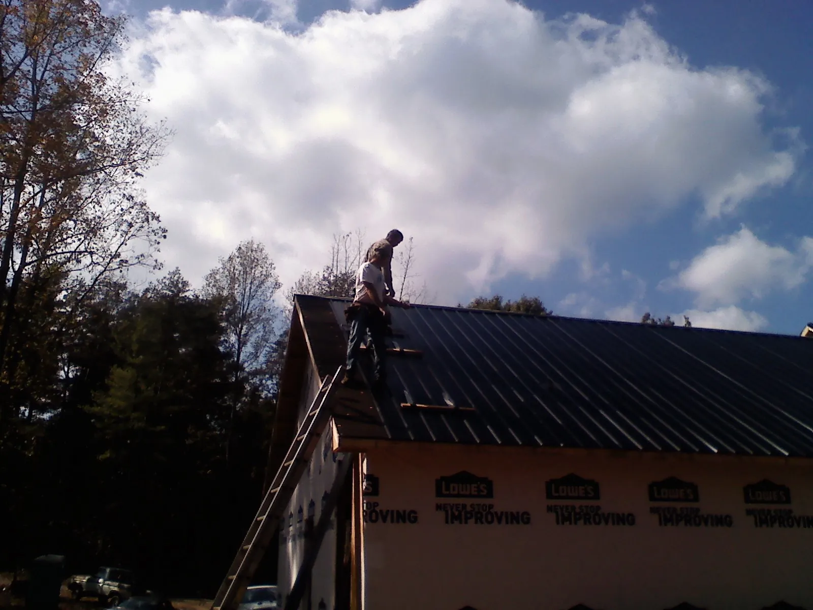 Roofer fastening dark metal panels high against a cloudy sky, from a Roof Inspection job in Burkeville